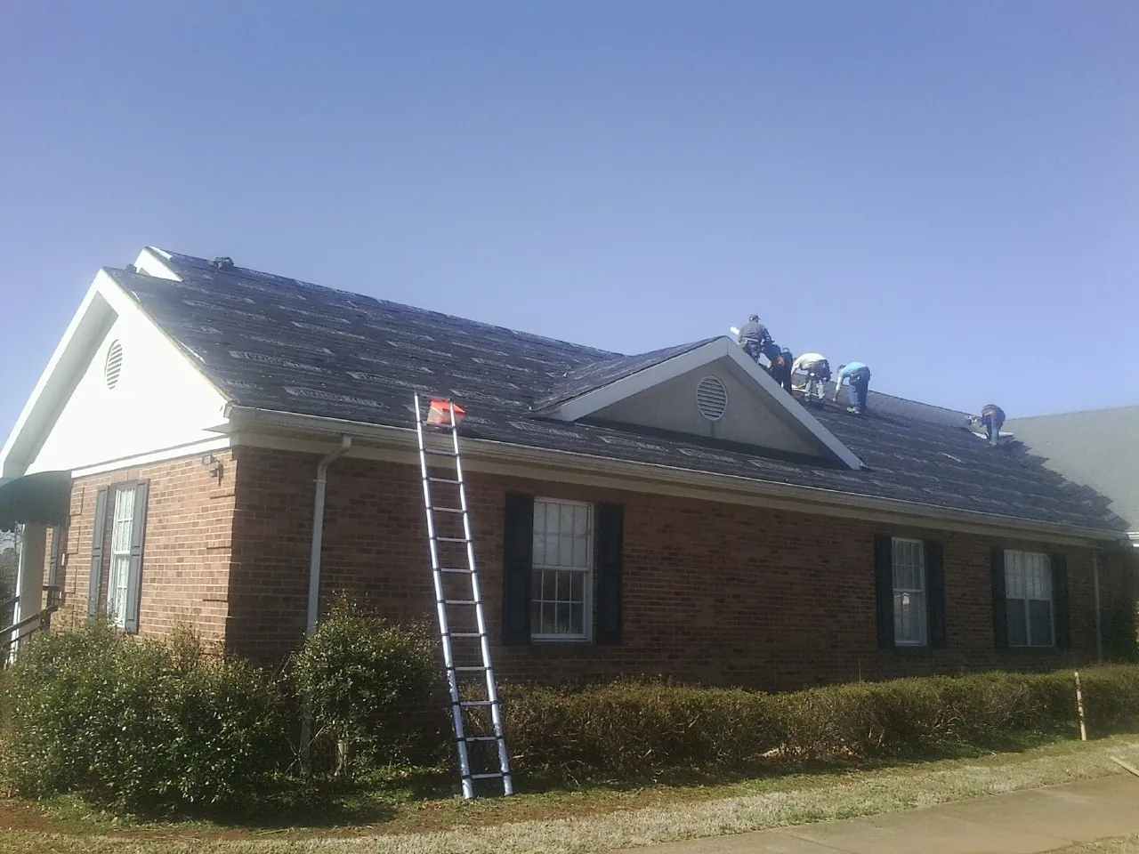 Crew tearing shingles off a brick ranch roof with a ladder set — Metal Roof Repair work by our crew in Grangeville