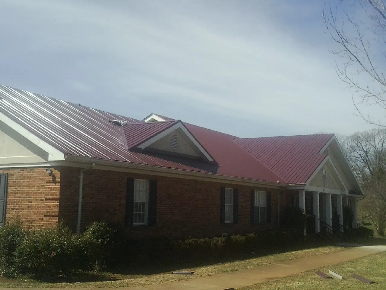 Red metal roof with gabled entries on a long brick building, from a Hail Damage Roof Repair job in Grangeville