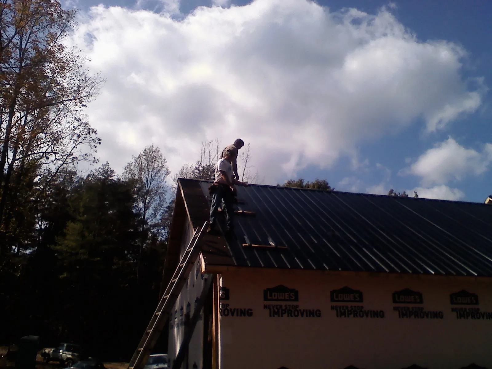 Roofer fastening dark metal panels high against a cloudy sky, from a Roof Inspection job in Grangeville