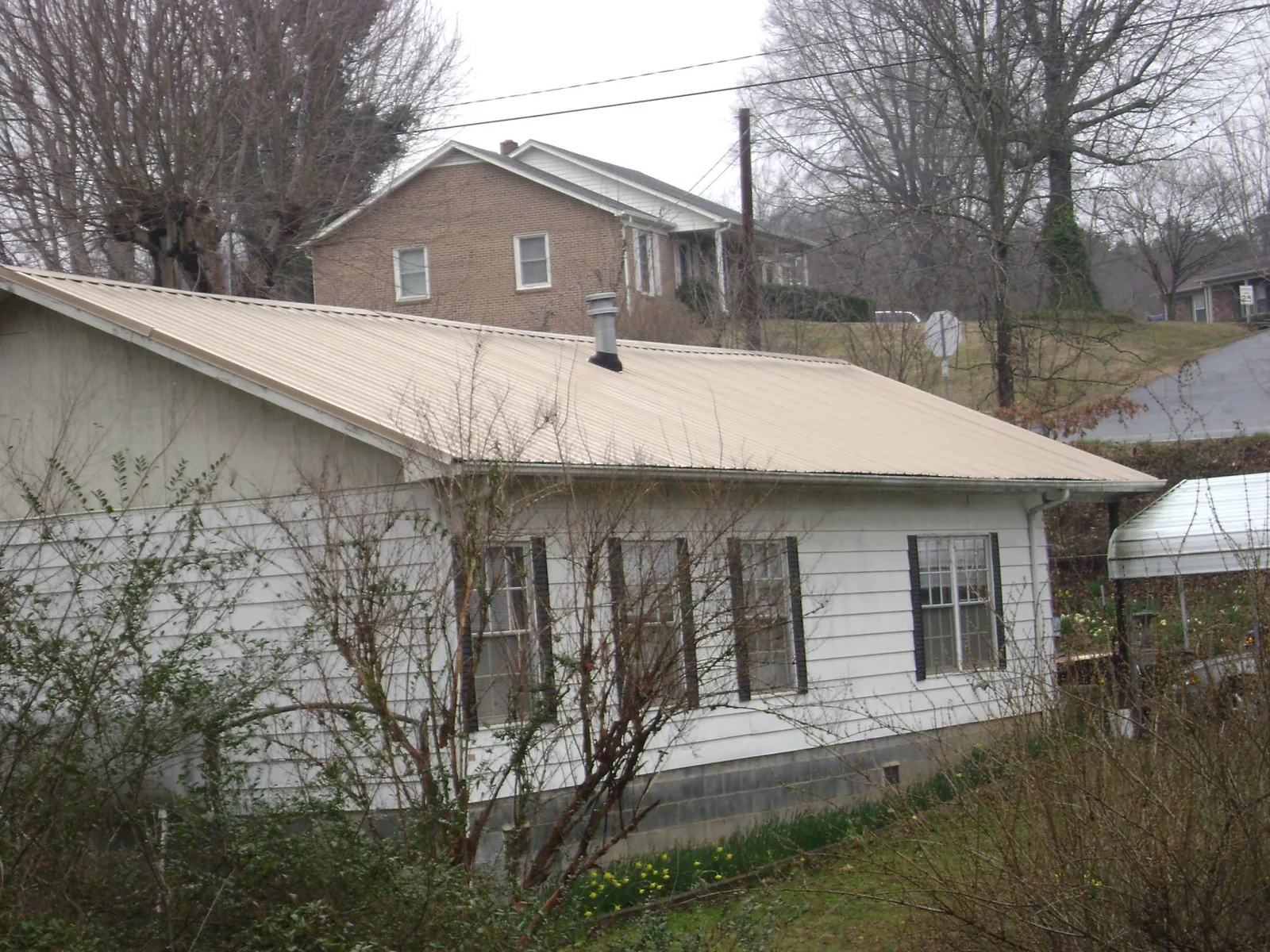 Tan metal roof on a white sided house set into a hillside — Commercial Roofing by Roofing Brothers in Grangeville